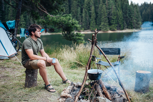Young man sitting by the campfire enjoying the beauty of nature on a camping vacation.