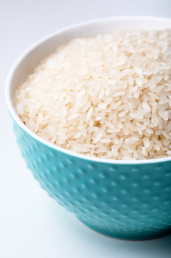 Bowl of raw organic rice on white background.  Blue bowl full of rice on white background.