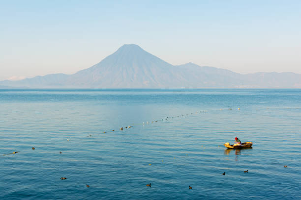 Indigenous Maya fisherman on the Atitlan Lake by Panajachel city with volcano in background, Guatemala.