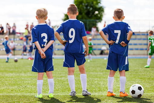 A medium, portrait shot of a young boy while playing football for a children's team in the North East of England. He is standing, looking and smiling at the camera on the sports field wearing a sports bib.