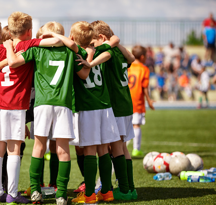 Group of children huddling. Soccer fans at the stadium in the background. Youth soccer football team group photo. Happy boys soccer players kicking tournament. School boys in green jerseys