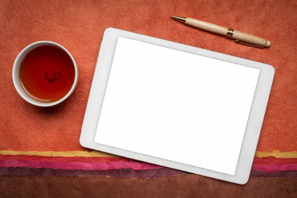 mockup of digital tablet with a blank isolated screen (clipping path included), flat lay with a cup of tea against abstract paper landscape
