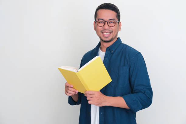 istock Adult Asian man smiling friendly at the camera while holding a book 1453997245