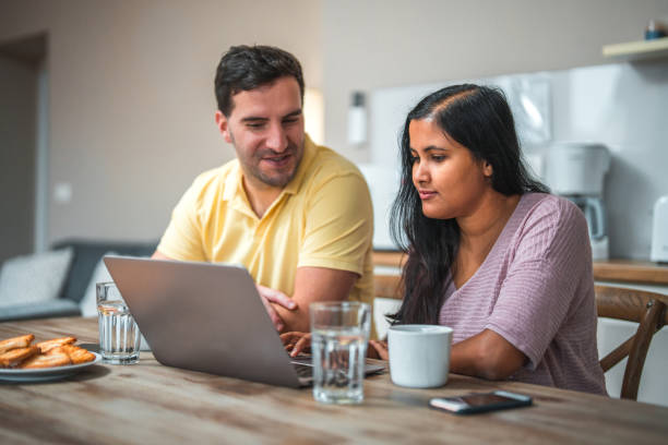 istock Caucasian Male And Indian Female Using Laptop In A Kitchen 1453997598
