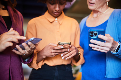Close-up of a group of diverse businesswomen looking at something on their smart phones while standing together in an office