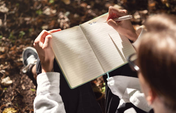 istock Opened notebook with handwriting text To Do, Person sitting on ground in park and writing notes in diary. 1454000396