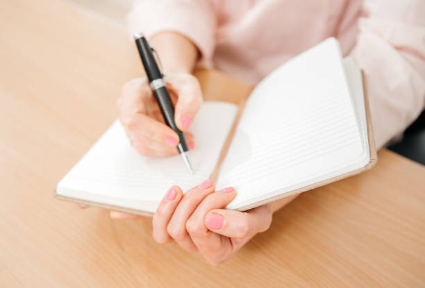 istock Close up of a woman's hands writing in a notepad placed on a wooden table, home office and work concept, plans and thoughts 1454003616