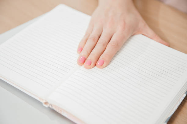 Close up of a woman's hands writing in a notepad placed on a wooden table, home office and work concept, plans and forecasts