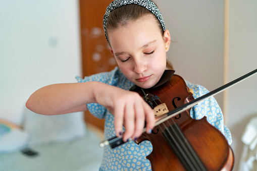 Cute girl playing violin in white bedroom with white curtain background. Musical and people lifestyles. Education and recreation concept. Back to school theme