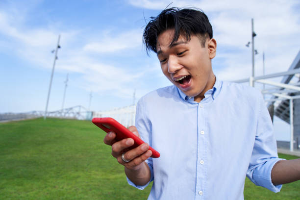 istock Close up of an excited Asian boy using smart phone gesturing surprise expression face 1454007658