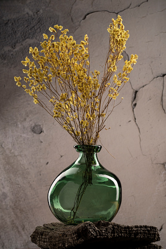 A vertical of a decorative vase with dried yellow flowers against the cracked wall background