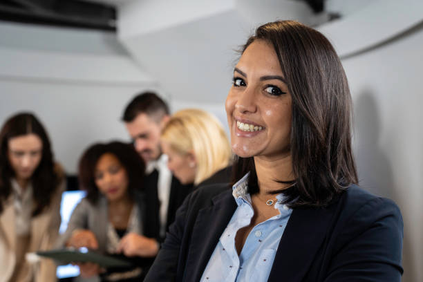 Smiling moroccan businesswoman working inside modern office with the multiethnic team behind her - Concept of leadership and teamwork achieving goals - Focus on eyes