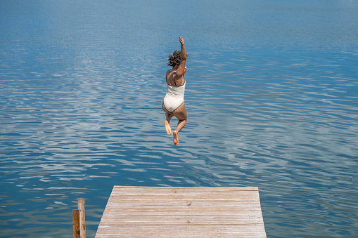 Rear view of an African woman jumping into the lake from wooden pier.