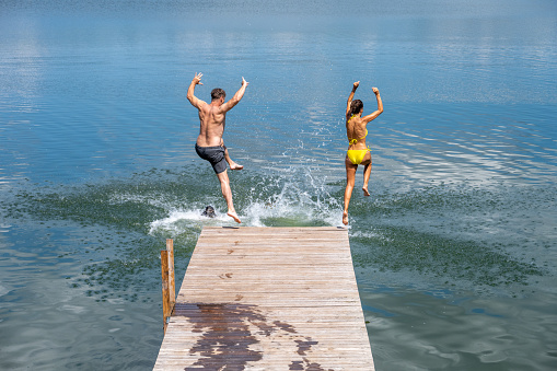 Middle aged couple enjoying their vacations and jumping into the lake from wooden pier.