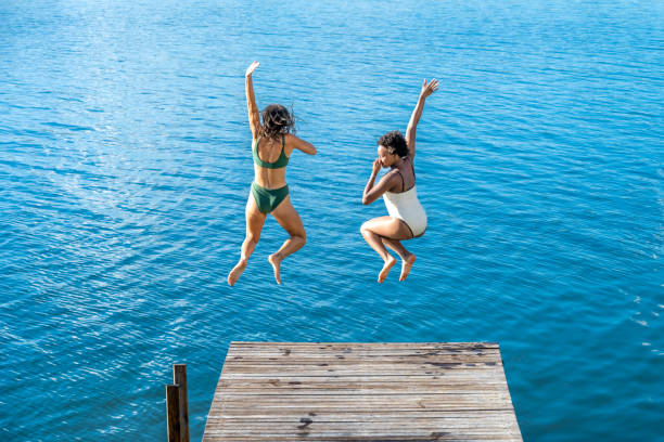 istock Two women enjoying their holiday while jumping into the lake 1454010151