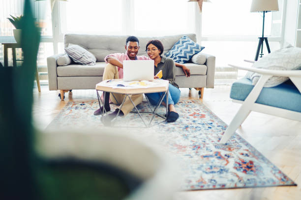 istock Cheerful black couple using laptop near sofa 1454012613