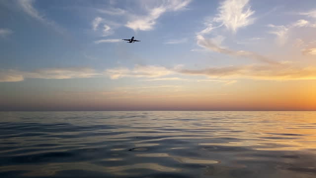 Airplane flying above the sea at sunset, low angle view