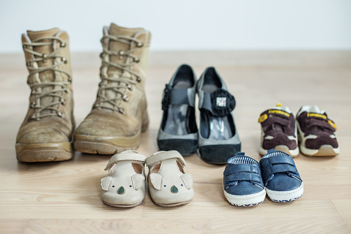 old worn military boots, women's shoes and lot of baby shoes on wooden floor. Military father and family concept. Copy space
