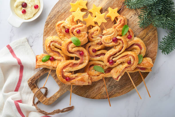 istock Christmas or New Year appetizer. Christmas tree shape puff pastry buns with cheese and ham. Group of Christmas tree shapes on wooden board. Festive idea for Christmas or New Year dinner. Top view. 1454019353