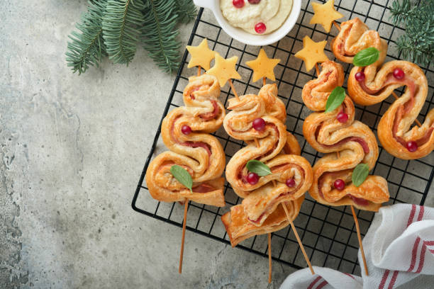 istock Christmas or New Year appetizer. Christmas tree shape puff pastry buns with cheese and ham. Group of Christmas tree shapes on stand for hot. Festive idea for Christmas or New Year dinner. Top view. 1454019362