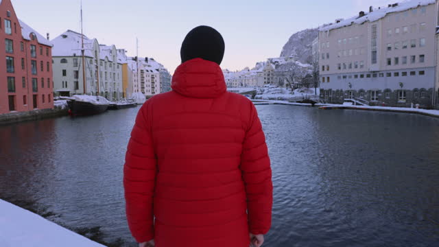 Rear view of man contemplating a view of Alesund city in snow from above in Norway