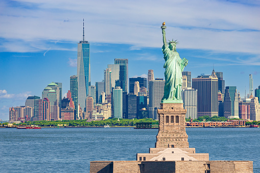 Statue of Liberty and New York City Skyline with Manhattan Financial District, Battery Park, Water of New York Harbor, World Trade Center, Empire State Building, Governors island and Blue Sky with Clouds. HDR image. Canon EOS 6D (full frame sensor) camera. Canon EF 70-200mm f/4L IS USM Lens.