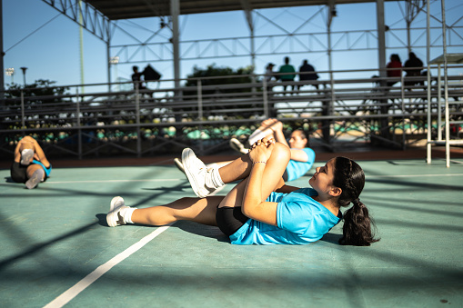 Teenage girl stretching with her team during warm-up at sport court