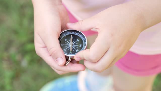 School age child, girl holding a simple compass in hands, seeking north, outdoors shot, object detail, closeup. Finding the right way, right direction, guidance, education and decisions concept