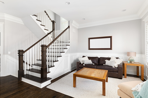 A bright, furnished living room near a staircase with wood banisters and steps, white rails, and board and batten walls.