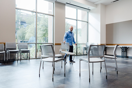 The mature man organizes chairs into a circle as he prepares for the recovery meeting that is going to take place in the empty conference room.