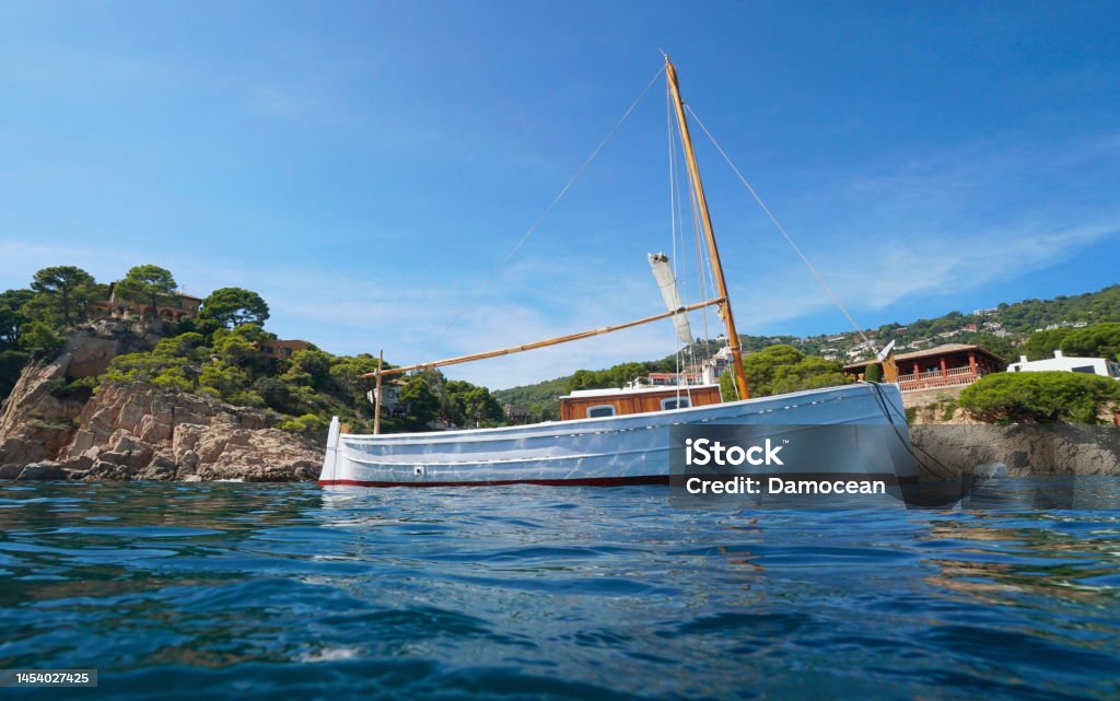 Typical Mediterranean boat seen from sea surface Spain Typical Mediterranean boat moored near rocky coastline with houses seen from sea surface, Spain, Costa Brava, Begur, Catalonia Baix Empordà Stock Photo