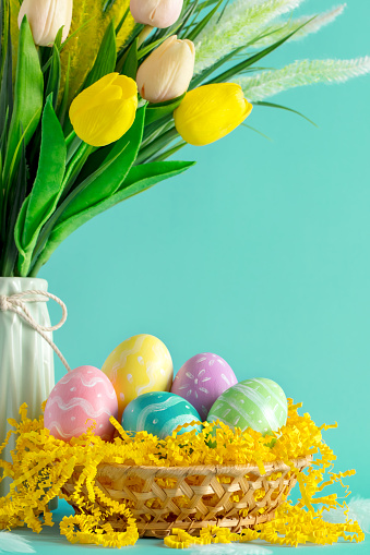 Multi colored hand-painted Easter eggs in a basket with the bouquet of tulips in a vase. Space for copy.