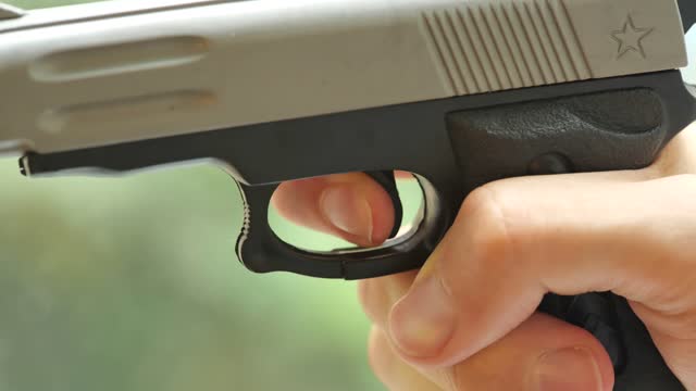 Man with shaky hands slowly pulling the trigger on a small cheap toy gun, object detail, closeup. Shooting a weapon, nervous shooter, gun safety laws rules, danger abstract concept, one person