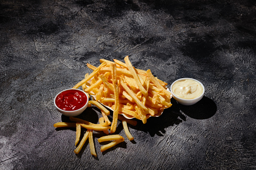 French fries in bowl on wooden boardFrench fries in fryer basket on dark background