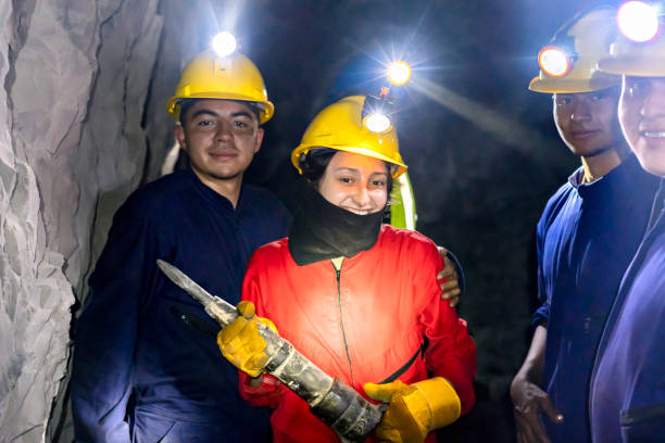 Little girl worker in a safety helmet with a tool on a light background.