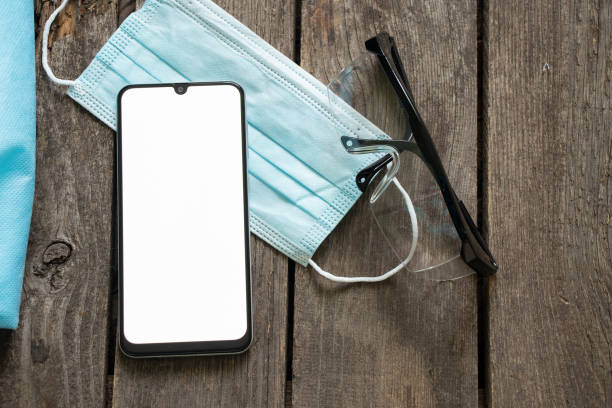 istock phone with blank white screen next to glasses and a medical mask on a table 1454047962