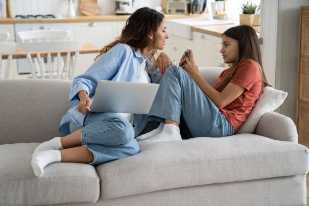 istock Mother and daughter using devices. Mom spying on kid on internet, spending time together at home 1454049527