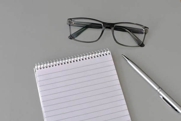 Flat display of a notepad, pen and a pair of glasses on a light grey background. Copy space. No people.
