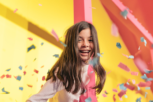 Happy girl on yellow background. Portrait of a beautiful girl having fun with sparkling confetti