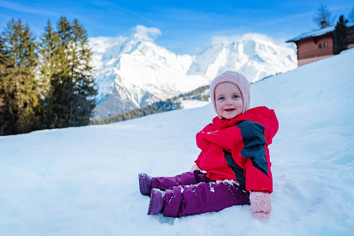 Side portrait of a happy young girl sit in winter outfit outside over snow mountains