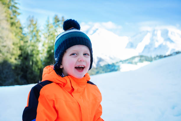 Close portrait of a laughing young boy in winter outfit outside over snow mountains