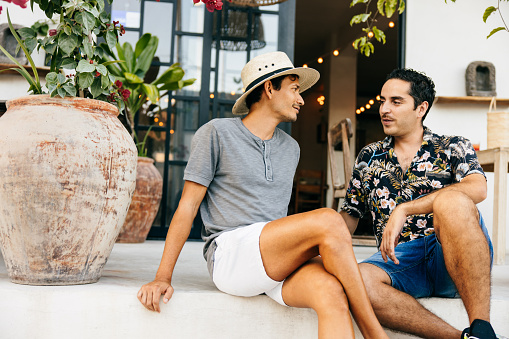 Smiling gay couple  talking while sitting in yard. Happy men are having leisure time. They are wearing casuals.