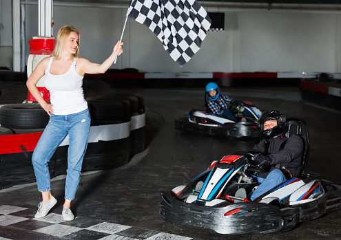 Happy woman with checkered race flag and man driving sport car for carting