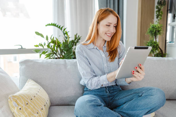 istock Young woman sitting on sofa and using digital tablet 1454062486
