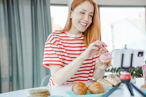 Young woman showing homamade sweets and talking in front of the camera for her Social Media followers