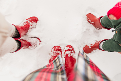 First-Person Downward View of a Woman Wearing Red Rubber Boots & a Christmas Tartan Plaid Coat While Standing With Her Two Kids Also Wearing Matching Red Rubber Boots in the Fresh White Fluffy Snow in Jackson, Ohio for Christmas in December 2022