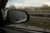 Rear-view mirror of car behind wet glass.