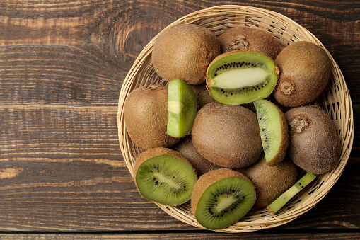 Delicious ripe many kiwi fruit and kiwi sectioned in a basket on a brown wooden table. top view. space for text