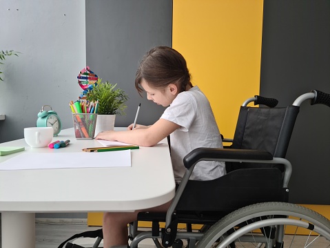 Disabled child schoolgirl with homework in class at school. Disabled girl draws at home
