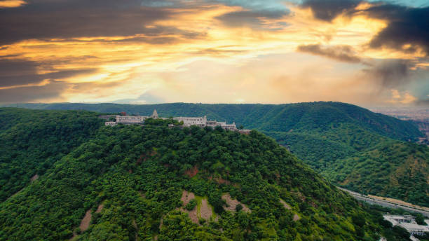 aerial drone shot flying towards the famous landmark chulgiri jain temple on agra jaipur road after ghat ki guni tunnel, white building perched atop lush green aravalli hill mountains stock photo